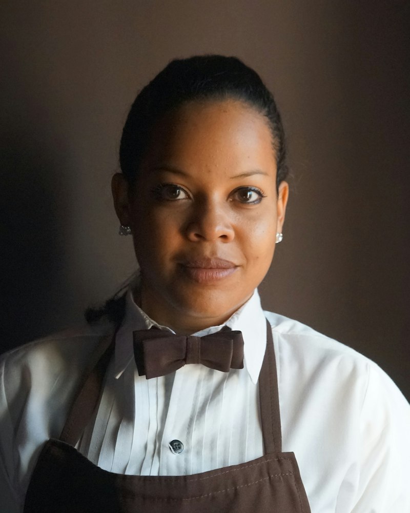 A server in a white shirt, bow tie and apron stands ready for service