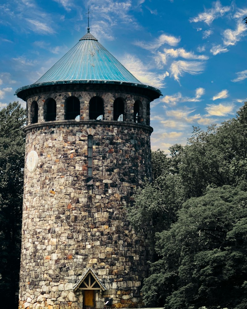 A stone tower with a green copper roof in a park under a blue sky
