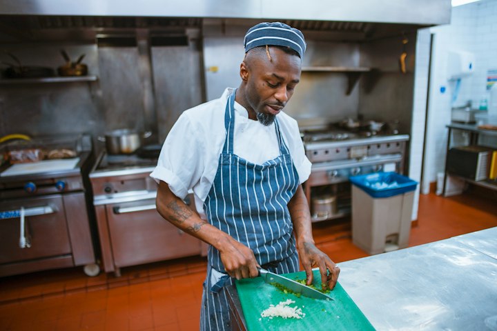 A cook in a striped apron chops garlic in a commercial kitchen