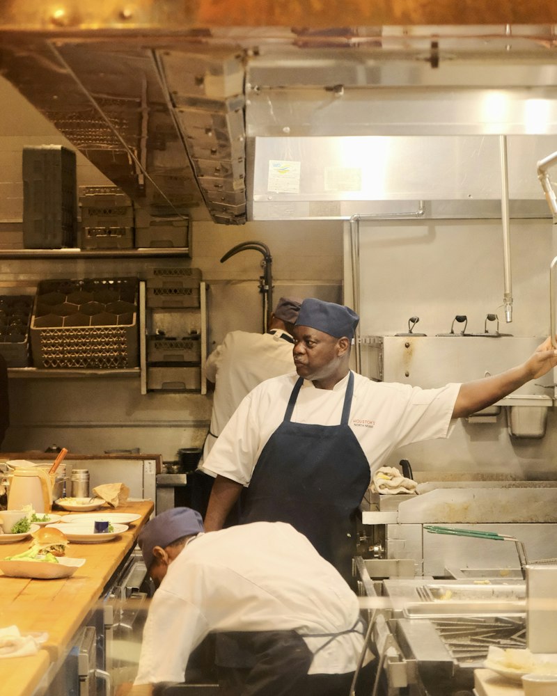 A cook in whites directs the kitchen while a teammate works the line