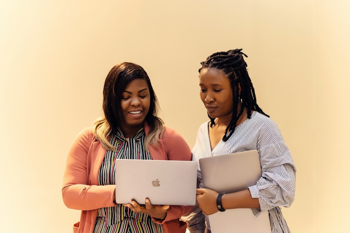 Two women look over a laptop together, one showing the other something
