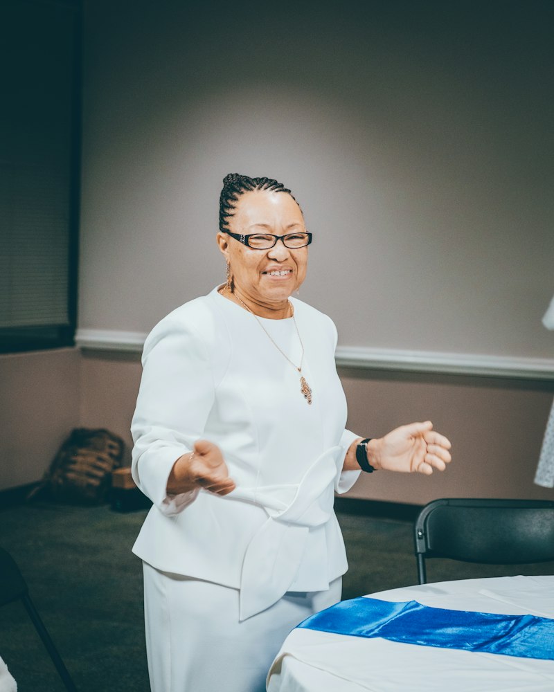 A facilitator in white smiles and gestures while speaking to a room