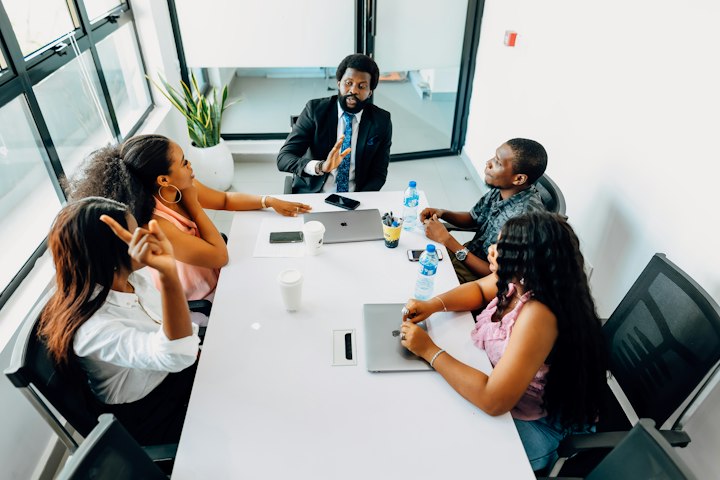 Five people meet around a white table in a bright office